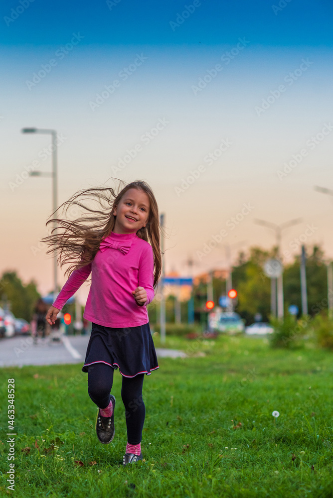 Beautiful little girl in a pink blouse is having fun on the city street.