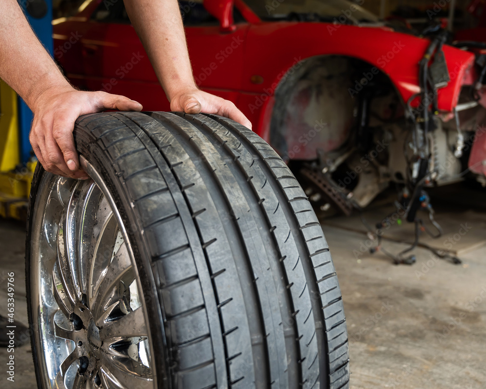 An auto mechanic holds a wheel of a car. Change of car tires according to the season An auto mechanic holds a wheel of a car. Change of car tires according to the season