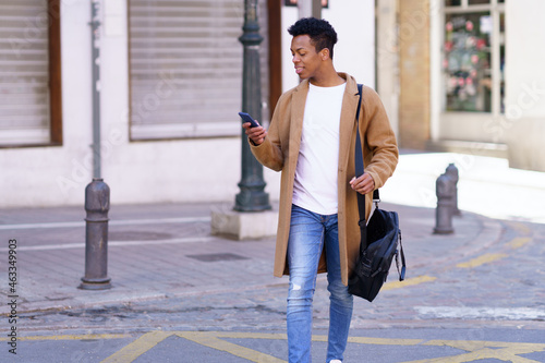 Young blackman looking at his smartphone while walking down the street. photo