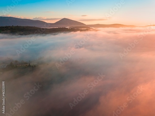 Fog spreads over the mountains at dawn. The sun rises on the horizon. Ukrainian Carpathians in the morning. Aerial drone view.