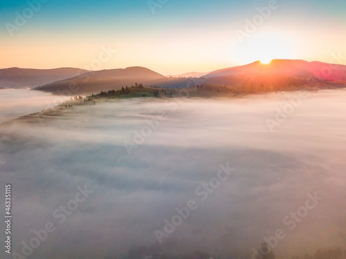 Fog spreads over the mountains at dawn. The sun rises on the horizon. Ukrainian Carpathians in the morning. Aerial drone view.