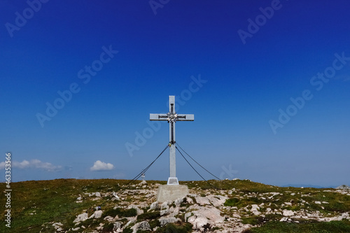 silver summit cross on a green mountain with rocks and deep blue sky