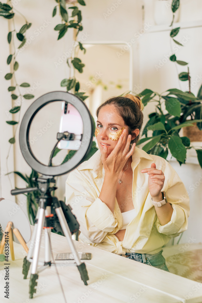 Young woman beauty blogger broadcasts live streaming to review makeup and cosmetic products on social media,applies patches under the eyes.Beauty and technology concept.Selective focus.
