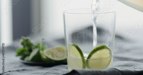 pour lemonade over lime slices in tumbler glass on linen cloth
