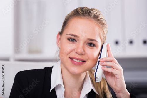Smiling woman talking on mobile phone and using laptop in office
