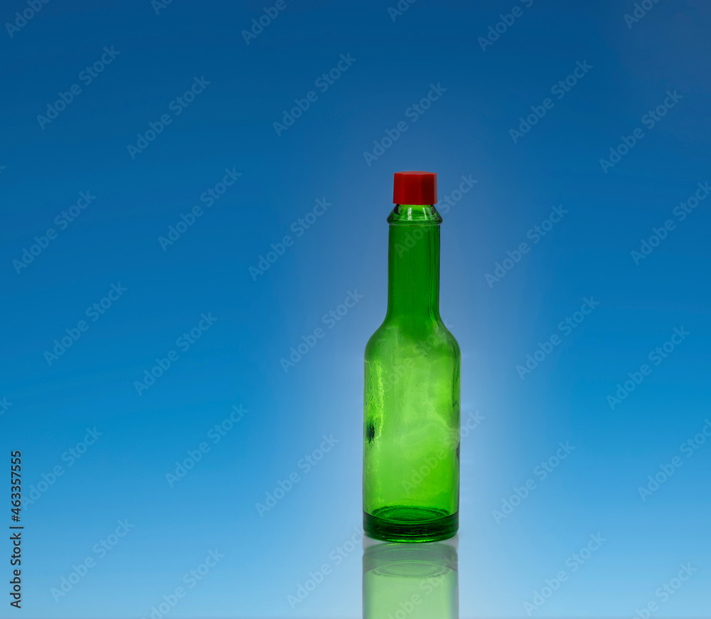Small empty green glass bottle with red cap without label on bright blue background Small empty green glass bottle with red cap without label on bright blue background