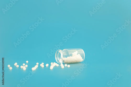 Close-up image of homeopathic globules in glass bottle on blue background. Homeopathy pharmacy, herbal, natural medicine, alternative homeopathy medicine, healthcare. Free space, copy space.