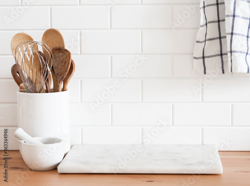 Stylish white kitchen background with kitchen utensils standing on wood countertop near white wall tiles