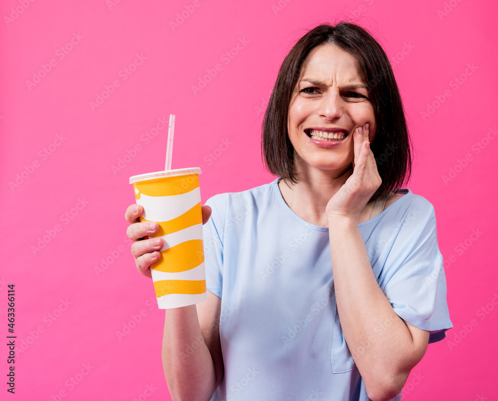 Young woman with sensitive teeth drinking cold water on color background Young woman with sensitive teeth drinking cold water on color background