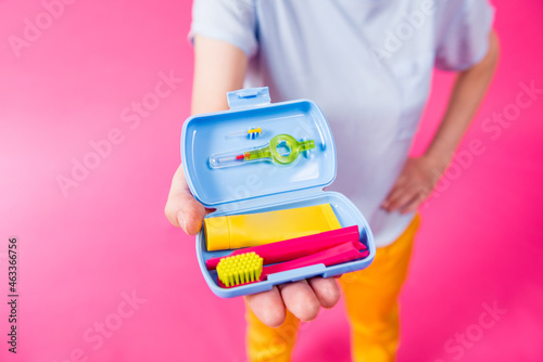 Beautiful girl uses a travel kit for dental care on a pink background