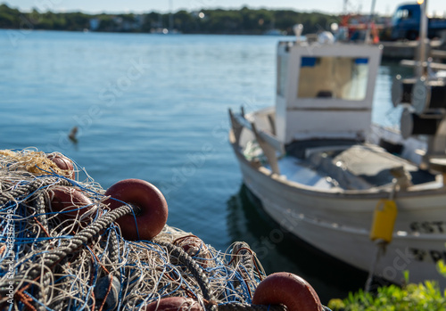 Close-up of fishing nets. In the background, out of focus, a fishing boat moored at the harbor in the Mallorcan town of Portocolom, Spain