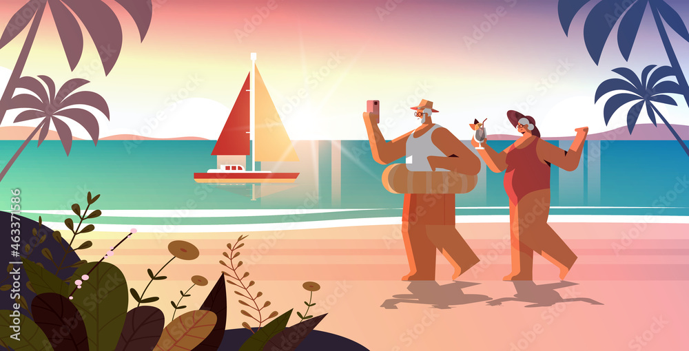 Obraz premium senior couple drinking cocktail and using smartphone on tropical beach grandparents having fun summer vacation