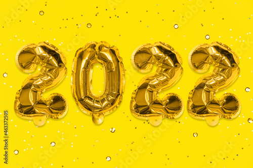 Golden foil balloons made numbers 2022 on a yellow background with golden sequins. New Year's card. Happy new year celebration party. Greetings and congratulation concept.
