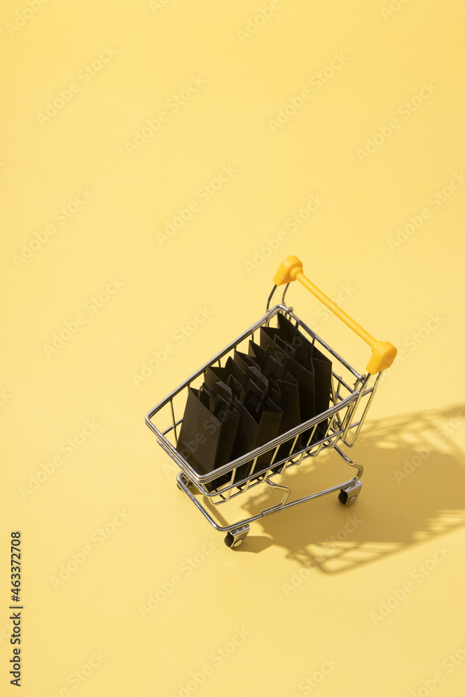 Miniature supermarket cart with shopping bags in black friday sale on yellow background Miniature supermarket cart with shopping bags in black friday sale on yellow background