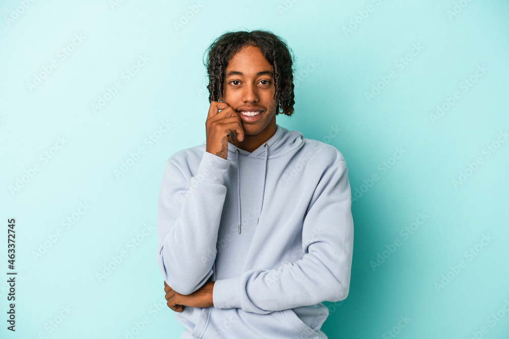 Young african american man isolated on blue background smiling happy and confident, touching chin with hand. Young african american man isolated on blue background smiling happy and confident, touching chin with hand.
