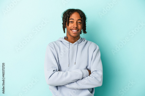Young african american man isolated on blue background who feels confident, crossing arms with determination.