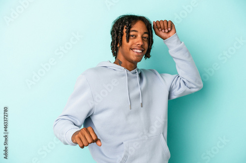 Young african american man isolated on blue background celebrating a special day, jumps and raise arms with energy. © Asier