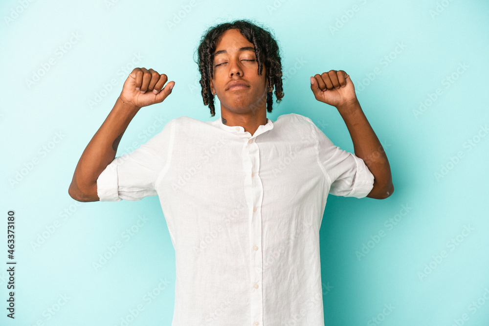 Fototapeta premium Young african american man isolated on blue background stretching arms, relaxed position.