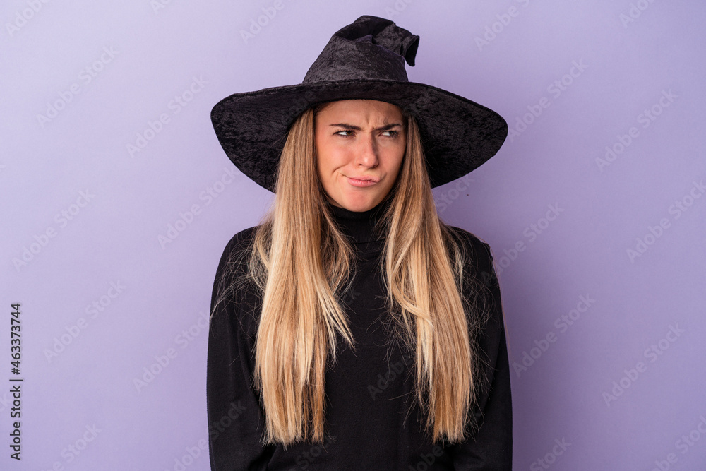 Young Russian woman disguised as a witch celebrating Halloween isolated on purple background confused, feels doubtful and unsure. Young Russian woman disguised as a witch celebrating Halloween isolated on purple background confused, feels doubtful and unsure.