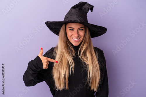 Young Russian woman disguised as a witch celebrating Halloween isolated on purple background person pointing by hand to a shirt copy space, proud and confident