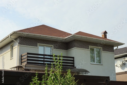 facade of a private gray house with an open brown wooden balcony on the background of the sky outside behind a fence