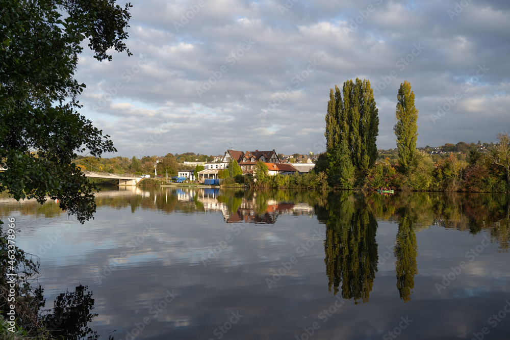 Fototapeta premium Blick über die Ruhr auf Essen Kupferdreh. Typische Herbstlandschaft im Ruhrgebiet. Bäume und Gebäude spiegeln sich im Wasser der Ruhr.