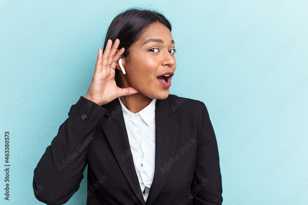 Young Venezuelan business woman isolated on blue background trying to listening a gossip. Young Venezuelan business woman isolated on blue background trying to listening a gossip.