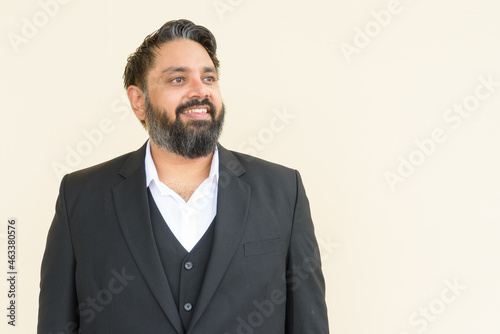 Portrait of handsome bearded Indian businessman against plain background