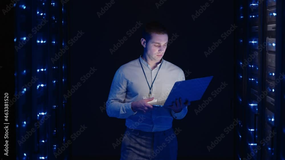 IT technician in data center digital server room controlling work of rack server cabinets with a tablet. Professional server engineer at work. Man technicians working in high tech server rack room