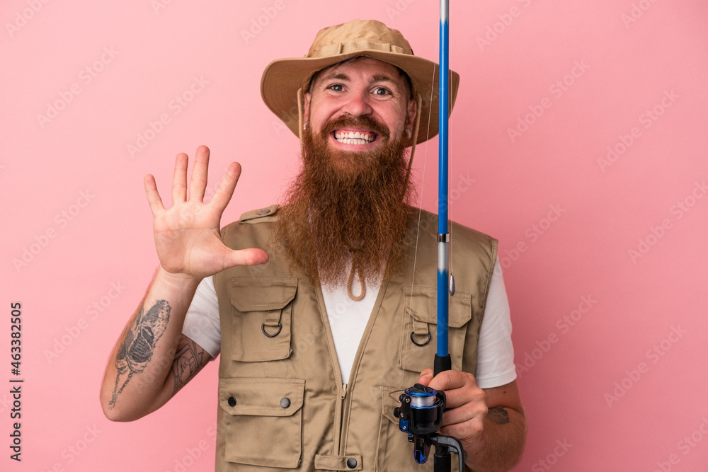 Young caucasian ginger fisherman with long beard holding a rod isolated on pink background smiling cheerful showing number five with fingers. Young caucasian ginger fisherman with long beard holding a rod isolated on pink background smiling cheerful showing number five with fingers.