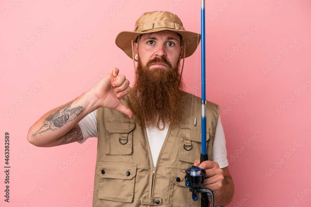 Young caucasian ginger fisherman with long beard holding a rod isolated on pink background showing a dislike gesture, thumbs down. Disagreement concept. Young caucasian ginger fisherman with long beard holding a rod isolated on pink background showing a dislike gesture, thumbs down. Disagreement concept.