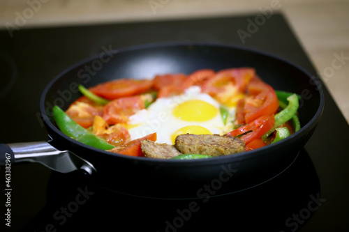 Frying pan with healthy food on a black hob.
