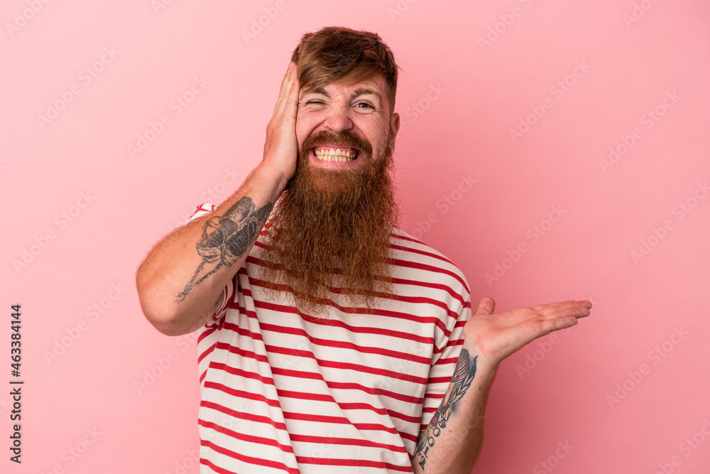 Young caucasian ginger man with long beard isolated on pink background holds copy space on a palm, keep hand over cheek. Amazed and delighted. Young caucasian ginger man with long beard isolated on pink background holds copy space on a palm, keep hand over cheek. Amazed and delighted.
