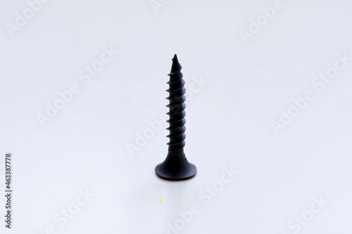 Single black screw standing on white underground