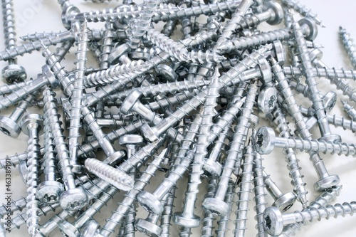 Pile of regular silver screws laying on white background