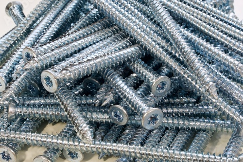 Closeup of pile of long silver screws for windows or frames on white background