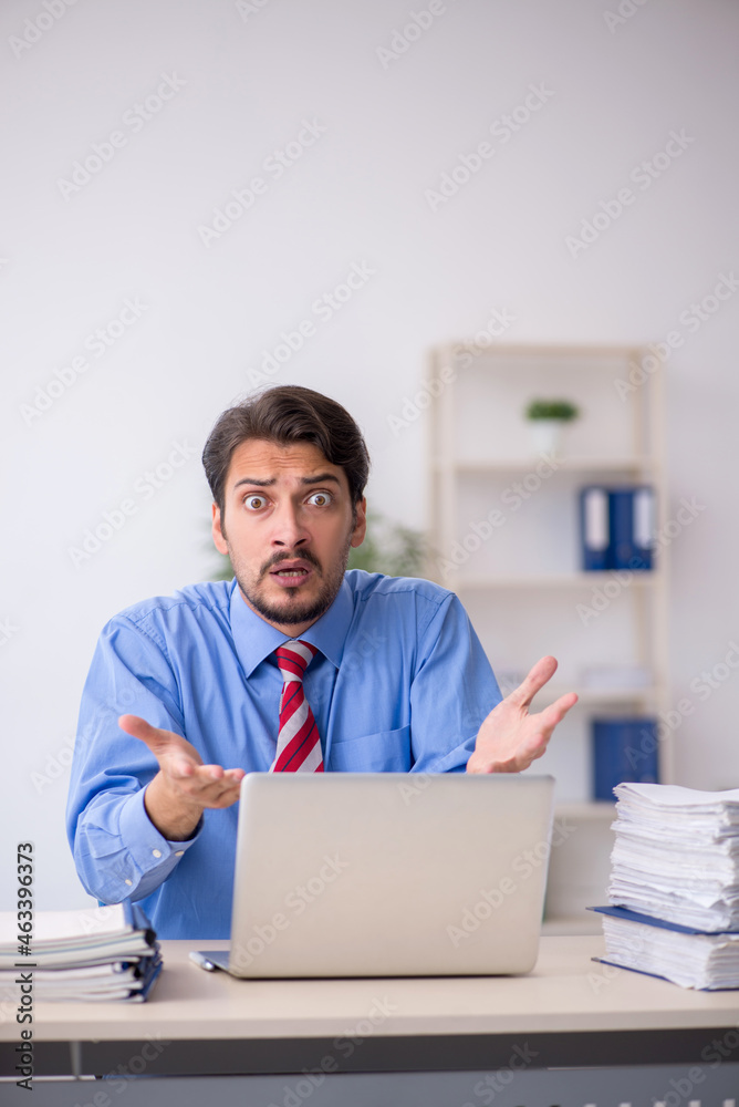 Young male employee unhappy with excessive work in the office Young male employee unhappy with excessive work in the office