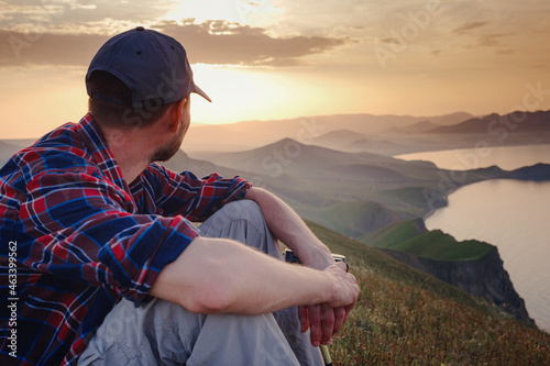 Confident man sitting and enjoying view in hilly landscape far from people. Tourist photographer is relaxing in nature during sunset. Adventure, Travel and Hike concept.