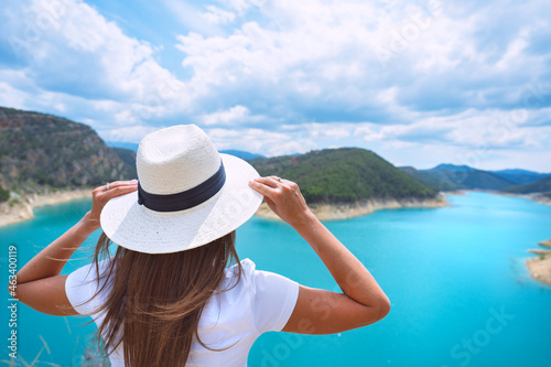 Woman tourist in white clothes and sun hat enjoying nature and great view of lake with pure blue water in Spain. Summer vacation in nature reserve