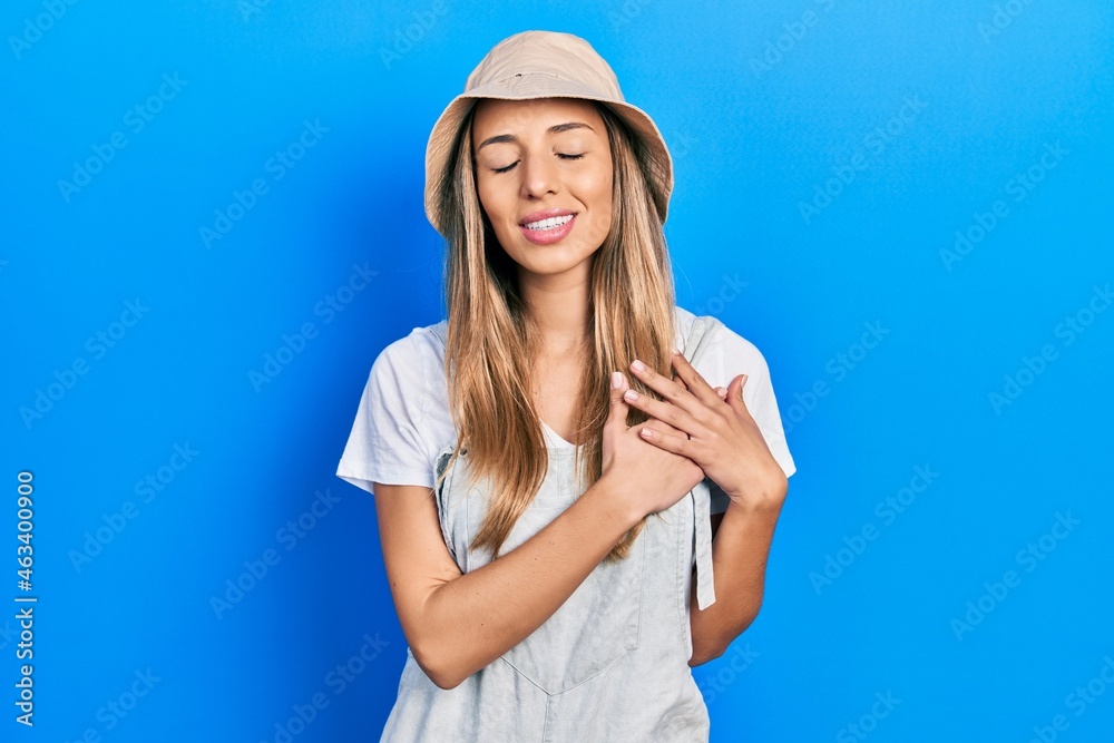Beautiful hispanic woman wearing explorer hat smiling with hands on chest with closed eyes and grateful gesture on face. health concept. Beautiful hispanic woman wearing explorer hat smiling with hands on chest with closed eyes and grateful gesture on face. health concept.