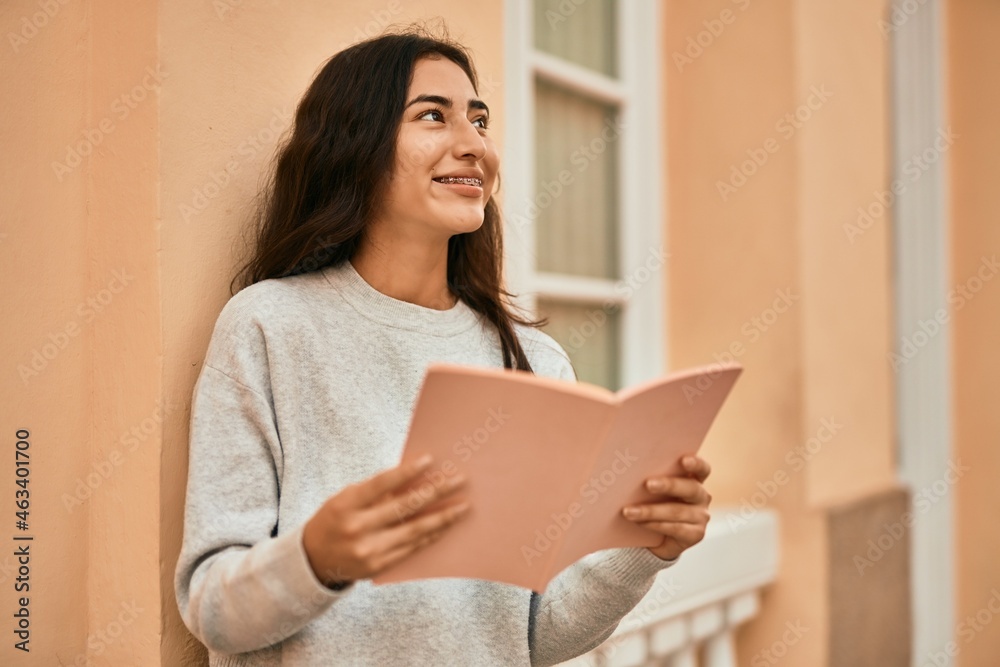 Young middle east student girl smiling happy reading book at the city. Young middle east student girl smiling happy reading book at the city.