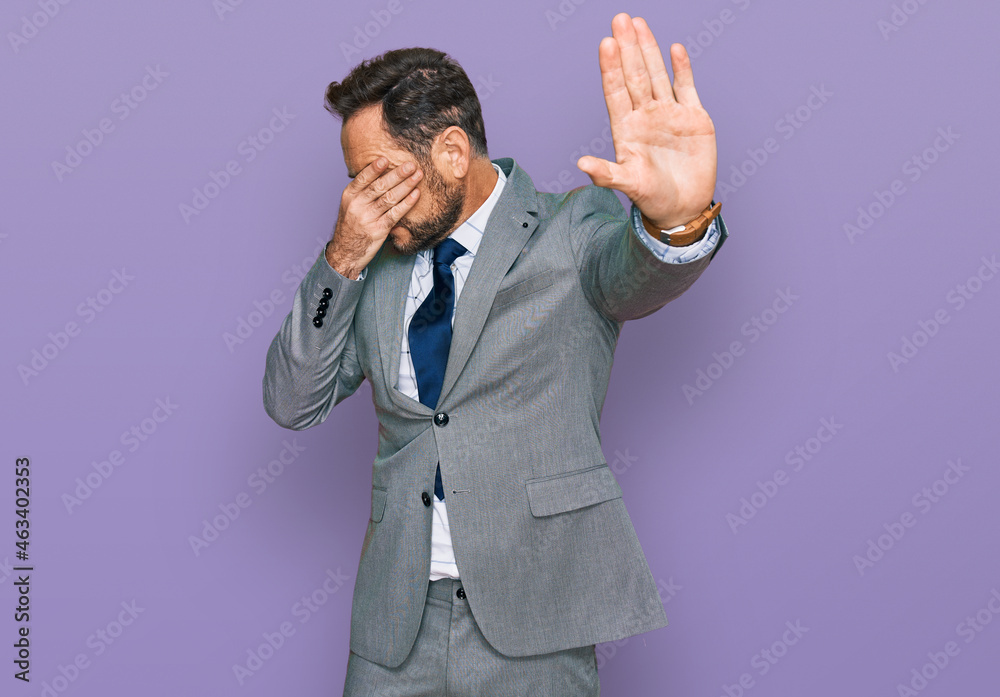 Middle age man wearing business clothes covering eyes with hands and doing stop gesture with sad and fear expression. embarrassed and negative concept. Middle age man wearing business clothes covering eyes with hands and doing stop gesture with sad and fear expression. embarrassed and negative concept.