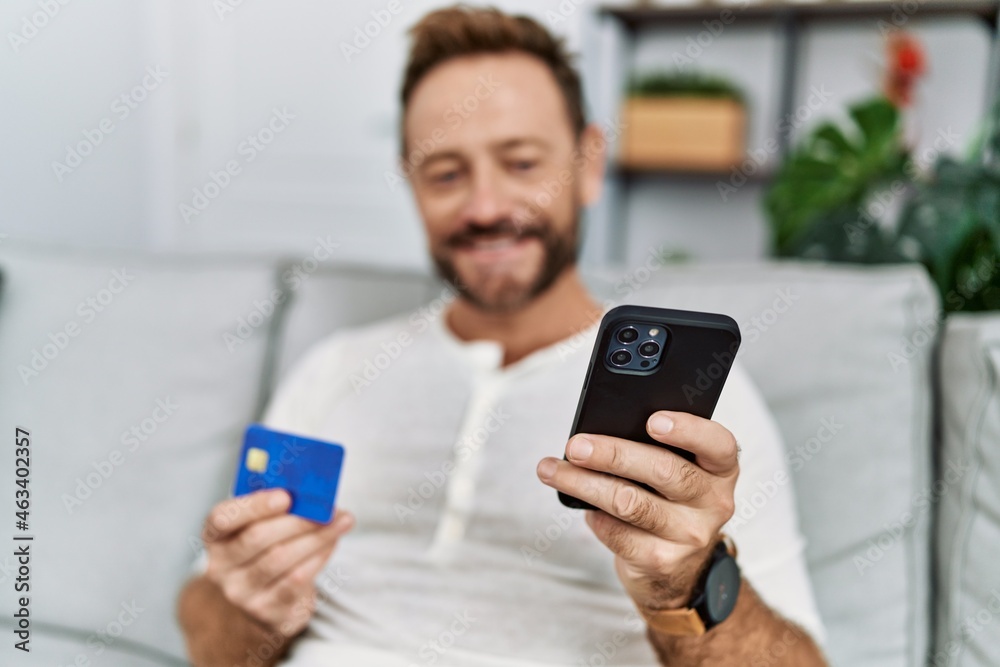 Middle age hispanic man using smartphone and credit card at home Middle age hispanic man using smartphone and credit card at home