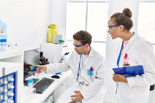 Man and woman wearing scientist uniform using computer working at laboratory