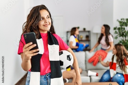 Group of young women watching and supporting soccer match. Hispanic woman smiling happy and using smartphone at home.