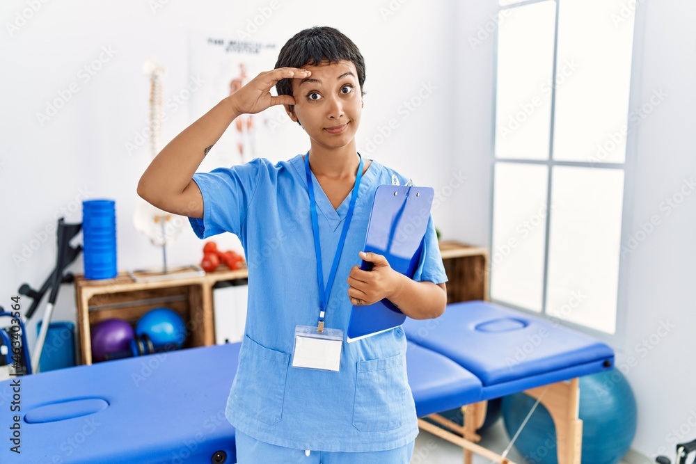 Obraz premium Young hispanic woman with short hair working at pain recovery clinic worried and stressed about a problem with hand on forehead, nervous and anxious for crisis