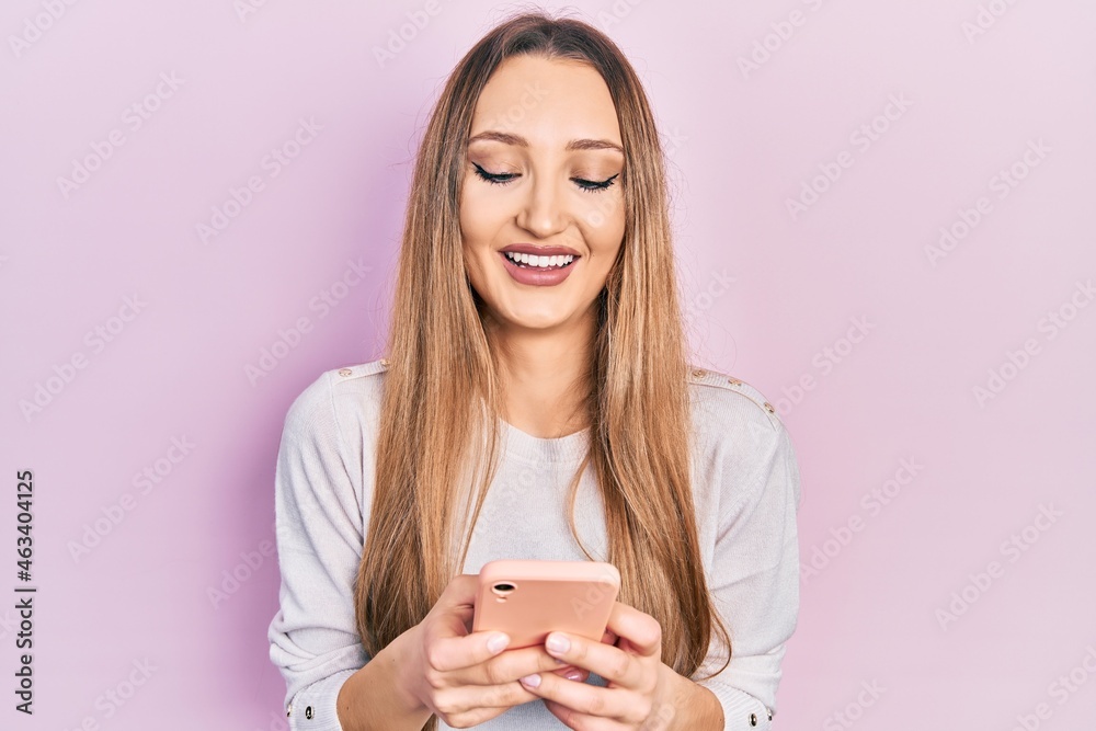 Young blonde girl using smartphone typing message smiling and laughing hard out loud because funny crazy joke. Young blonde girl using smartphone typing message smiling and laughing hard out loud because funny crazy joke.