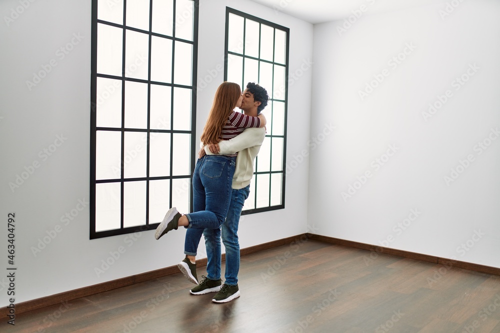 Young hispanic couple kissing and hugging standing at empty new home.