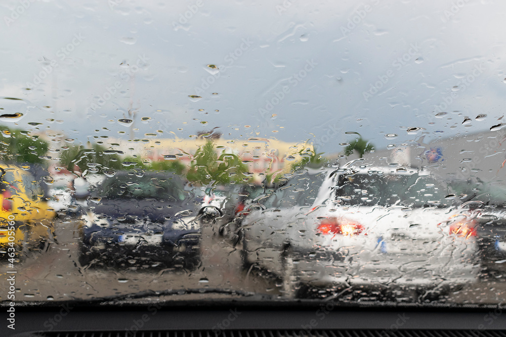 Fototapeta premium Raindrops on the window glass with outline of a car and a person