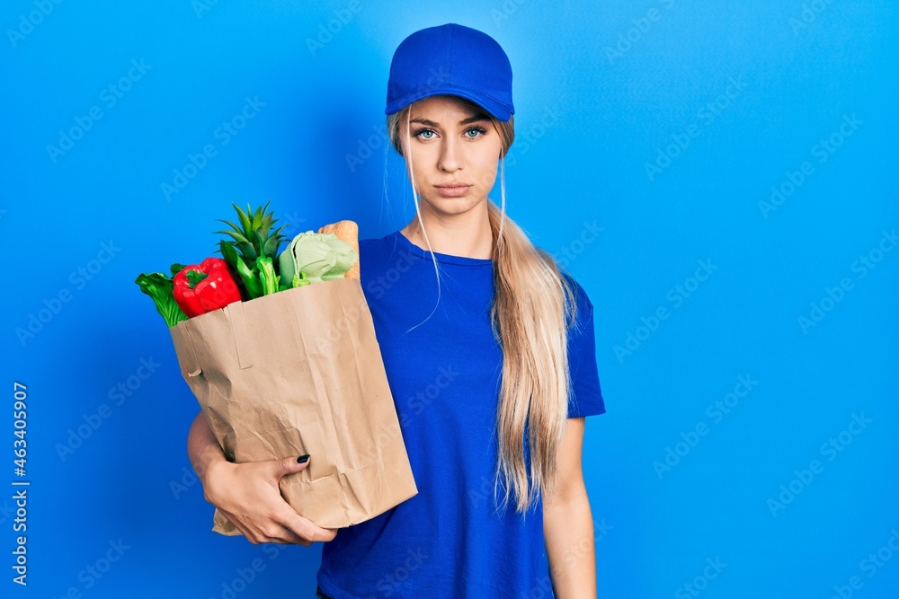 Young caucasian woman wearing courier uniform with groceries from supermarket skeptic and nervous, frowning upset because of problem. negative person. Young caucasian woman wearing courier uniform with groceries from supermarket skeptic and nervous, frowning upset because of problem. negative person.